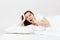 Calm young brunette woman lying in bed with white sheet, pillow, blanket on white background. Surprised beauty female
