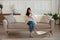 Calm young woman houseowner sitting on couch using mobile phone