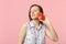 Calmed young woman in summer clothes keeeping eyes closed holding fresh ripe red apple fruit  on pink pastel