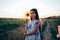 Calmy beautiful brunette teen girl standing among the field with sunflower near her head, wearing dress with flowers