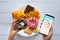 Calories counting and food control concept. woman using Calorie counter application on her smartphone with doughnut in hand