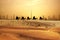 Camel caravan on sand dunes on Arabian dessert with Dubai skyline at sunset