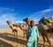 Cameleer (camel driver) with camels in dunes of Thar desert. Raj