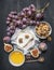 Camembert cheese on old dark wooden table with a bowl of walnuts, honey, a vintage table knife, cut figs and branch of grapes, top