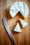 Camembert cheese with a triangular slices and a dirty knife on a wooden board