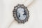 Cameo brooch, which is a side portrait of a woman, with small crystals around the edges on a white background.