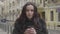 Camera approaching slowly to face of charming Caucasian girl smiling. Brunette young woman posing on city street on