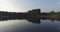 Camera flight over the lake, clear like a mirror. It reflects the trees on the shore, green grass, wooden house and blue