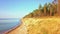 Camera flying up between sea and steep bank with a pine forest