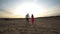 Camera following to young pair holding hands and walking through desert. Couple of lovers going on sand at sunset