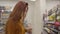Camera following young pretty redhead woman choosing beverage in supermarket. Concentrated beautiful girl selecting