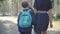 Camera follows brunette little girl walking along sunny schoolyard with unrecognizable mother. Back view of schoolgirl