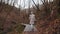 Camera follows happy photographer woman in white winter coat walking down mysterious autumn forest path slow motion.