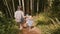 Camera follows happy young mother together with two little children walking down a steep exotic forest path slow motion.