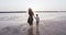 Camera follows happy young mother walking along sea beach with little boy child at stunning golden sunrise slow motion.