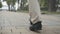 Camera follows male feet in boots walking along alley in spring or autumn park on cloudy overcast day. Unrecognizable