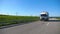 Camera follows to truck with cargo trailer driving on highway transporting goods at summer day. White lorry riding