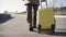 Camera follows unrecognizable elegant man walking with yellow suitcase along countryside road. Confident businessman