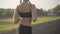 Camera follows young Caucasian jogger training in sunlight outdoors. Confident woman launching app on smart watch and