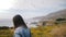 Camera follows young millennial girl walking down amazing Big Sur ocean rocky coastline covered with lush yellow flowers
