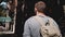 Camera follows young relaxed tourist man with backpack walking along shady summer New York city street with coffee.