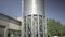 Camera goes down along enormous stainless steel cement storage silo with clear blue sky at the background. Wide shot of