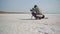 camera movement around cameraman operator at work. man filming using camera on tripod sitting on white salty beach of