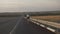 The camera moves behind a cyclist on a road bike riding on the side of an empty highway. A man on a sports bike rides