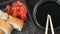 Camera moves zooms. Stylishly laid sushi set on a black wooden background next to soy sauce and Chinese bamboo sticks
