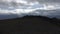 Camera moving towards a mountain top along the green slope. Clip. Aerial view of a green hill pick on cloudy sky