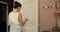 Camera peeps young brunette woman painting wooden door and dancing outdoors