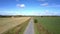 Camera rises above road between fields against blue sky