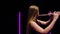 Camera rotates around charming female flutist in a black dress against a background of bright neon lights in a dark