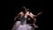 Camera rotates around two flexible ballerinas in black and white tutus move their hands dramatically against a backlit