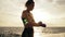 Camera round movement: female boxer wrapping hands with boxing wraps on the beach by the ocean standing against the sun