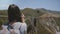 Camera slides right behind young tourist woman with backpack taking smartphone photo of iconic Bixby Canyon bridge.