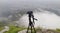 A camera on a tripod in the background of a valley above the clouds