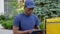 Camera zoom in afro-american man courier delivery sitting on bench uses tablet