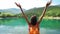 Camera zooming out view girl traveler standing with raising hands on background of beautiful mountain lake