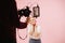 Cameraman filming young woman posing with wireless headphones. Over pink