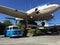 A camervan sittting under the wing of a old blue and white prop airliner in place on the side of the main highway in New Zealand