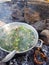 Camp cooking in the field on open fire - a big pan with vegtables and edible wild plants