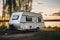 A camper parked next to a lake at sunset. Digital image.