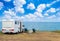 Camper van parked facing the sea from the top of a cliff under a blue sky with white clouds and two sun loungers overlooking the