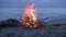 A campfire burns on a deserted sandy beach at the seashore in the evening