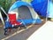 Campground Scene with a Tent, Walking Cane and Fishing Poles Leaning Against a Camp Chair