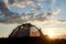 Camping at daybreak. The tent stands under blue sky with clouds in rays of evening sunlight