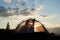 Camping at daybreak. The tent stands under blue sky with clouds in rays of morning sunlight