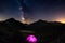 Camping with illuminated tent at high altitude on the Alps under starry sky and milky way reflected on lake. Adventure and explora