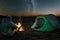 Camping man sits by the fire at night against the background of the starry sky. The concept of travel, tourism, camping